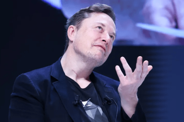 lon Musk speaking at an event, wearing a suit and looking confident